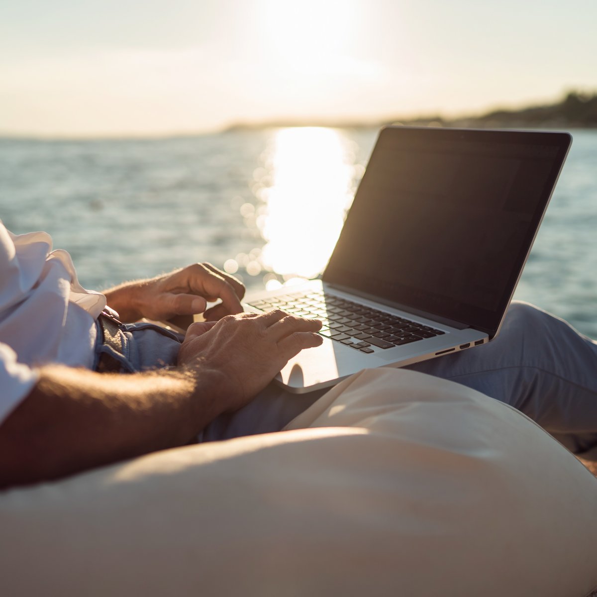 A person working on a laptop while being on the beach